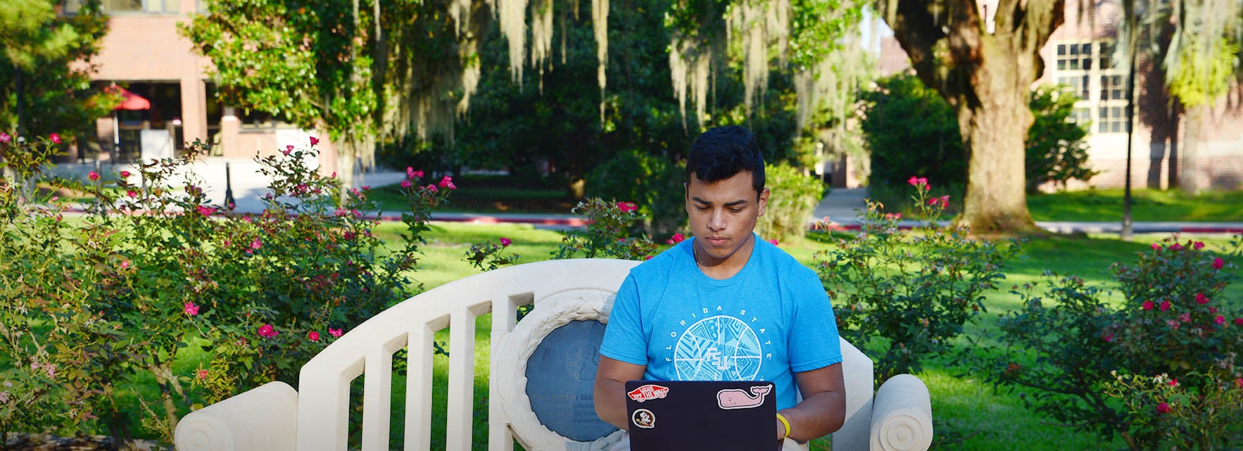 An FSU student works on a laptop while seated on a bench. An FSU student works on a laptop while seated on a bench.